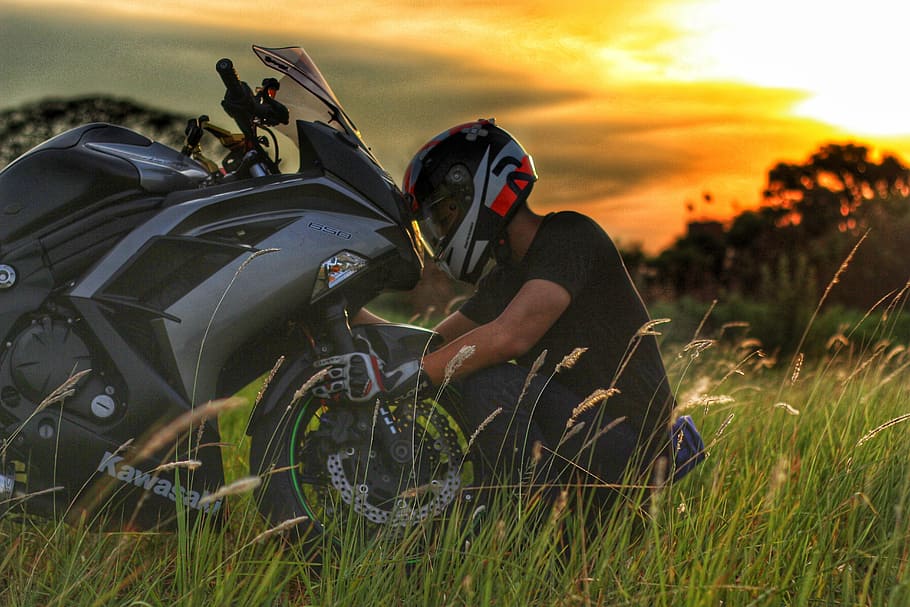 man sitting on grass field in front of gray sport bike photo, HD wallpaper