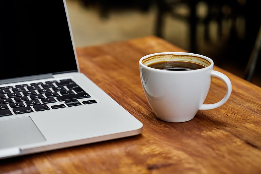 coffee filled white ceramic mug beside MacBook Pro on top of brown wooden table, HD wallpaper